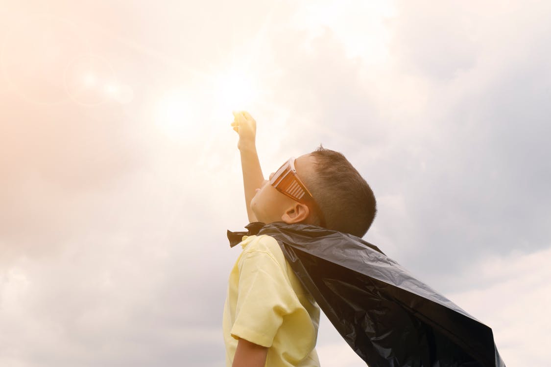 A young boy with a cape and sunglasses pretending to be a superhero.